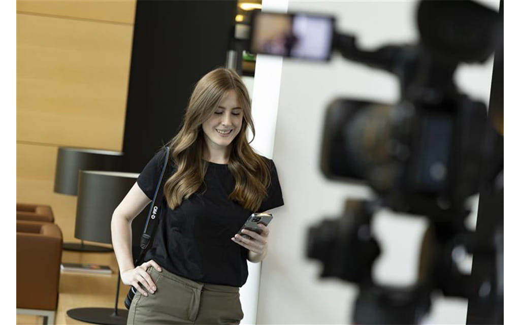 Frau vor der Kamera mit Handy in der Hand